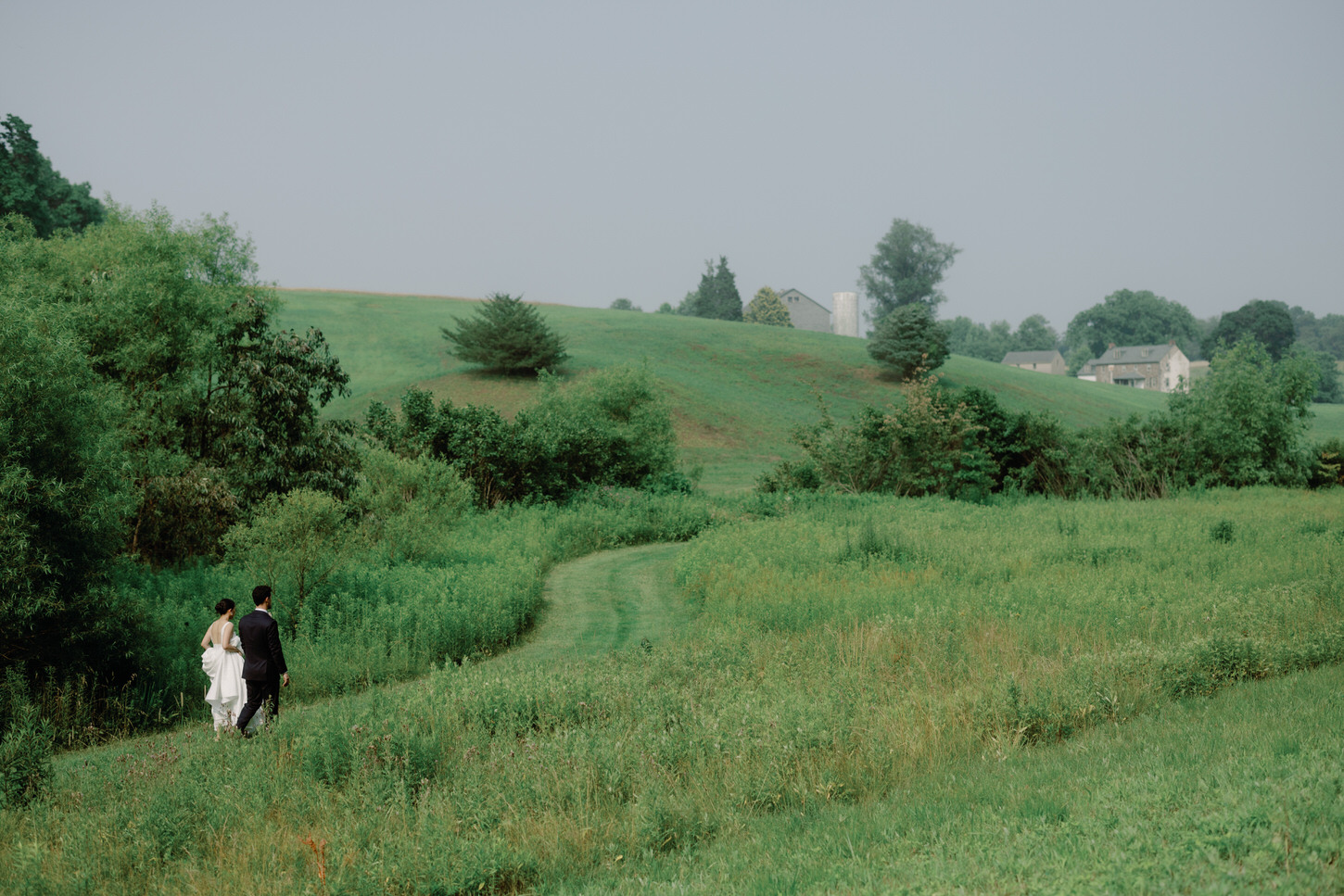 The bride and groom are intimately walking amidst sprawling greens in a whimsical wedding captured by Jenny Fu Studio NYC