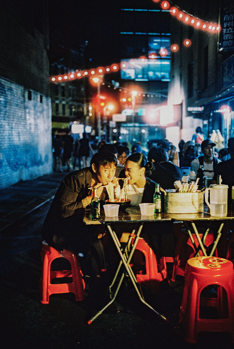 Bride and groom share a playful noodle moment at an outdoor Chinatown noodle shop in NYC.