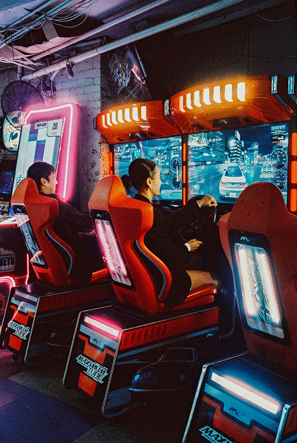 Bride and groom playing driving games in a neon-lit Chinatown arcade.