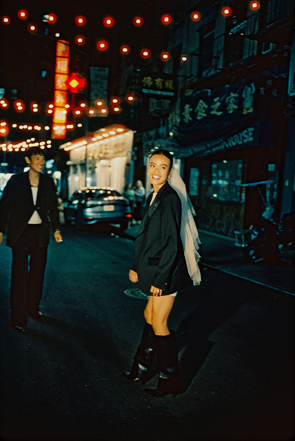 Bride in veil and black boots walking under Chinatown string lights during nighttime wedding shoot.