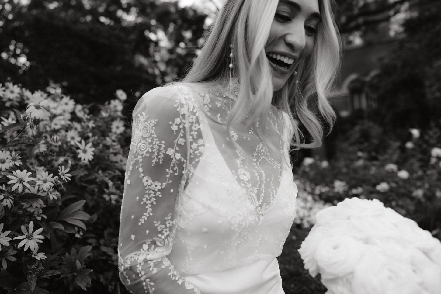 The happy bride is holding her flower bouquet in the midst of a garden, in a candid image captured by Jenny Fu Studio NYC. 