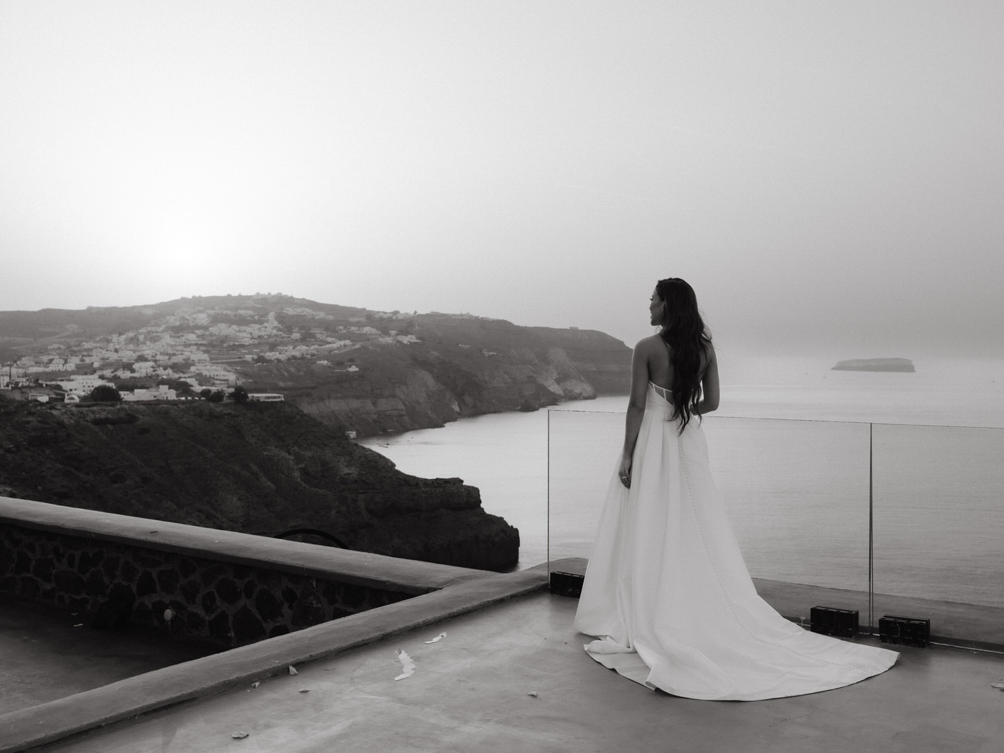 A photojournalistic portrait of the bride, overlooking a calm lake and a quaint village on the side, in Santorini, Greece, captured by Jenny Fu Studio.